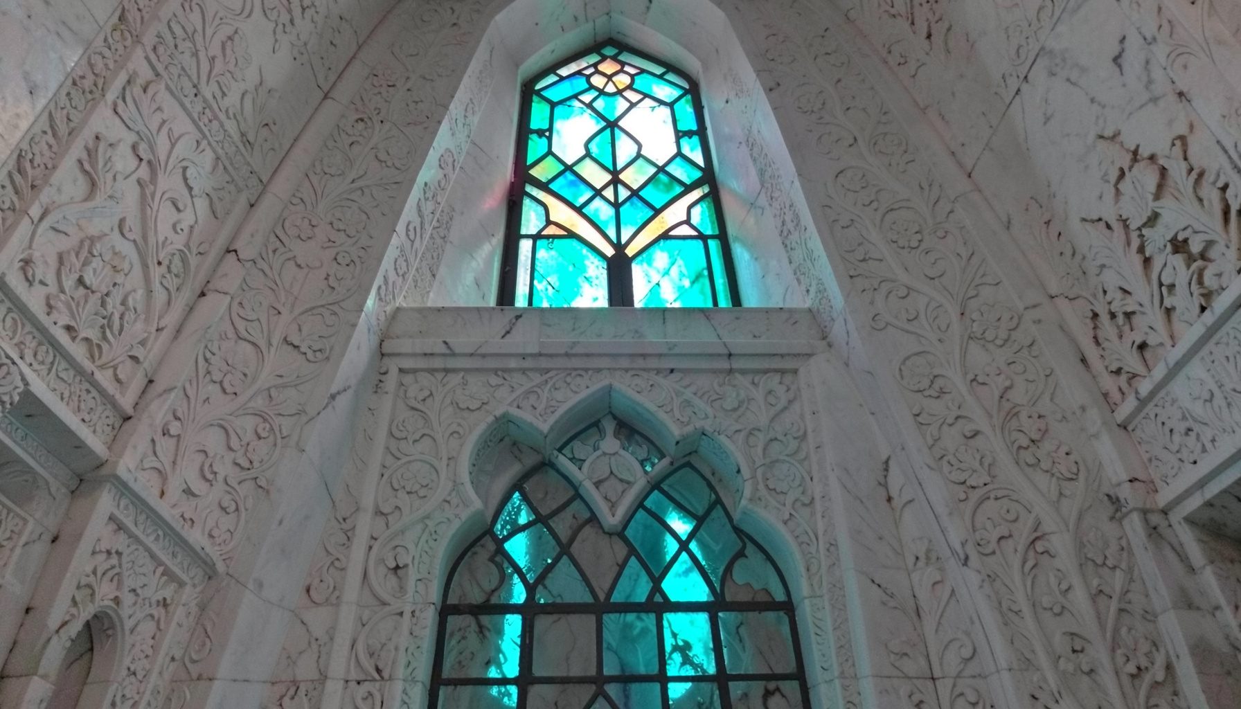 محراب مسجد من الرخام الأبيض المنقوش بزخارف نباتية، مع إضاءة ناعمة من نافذة علوية